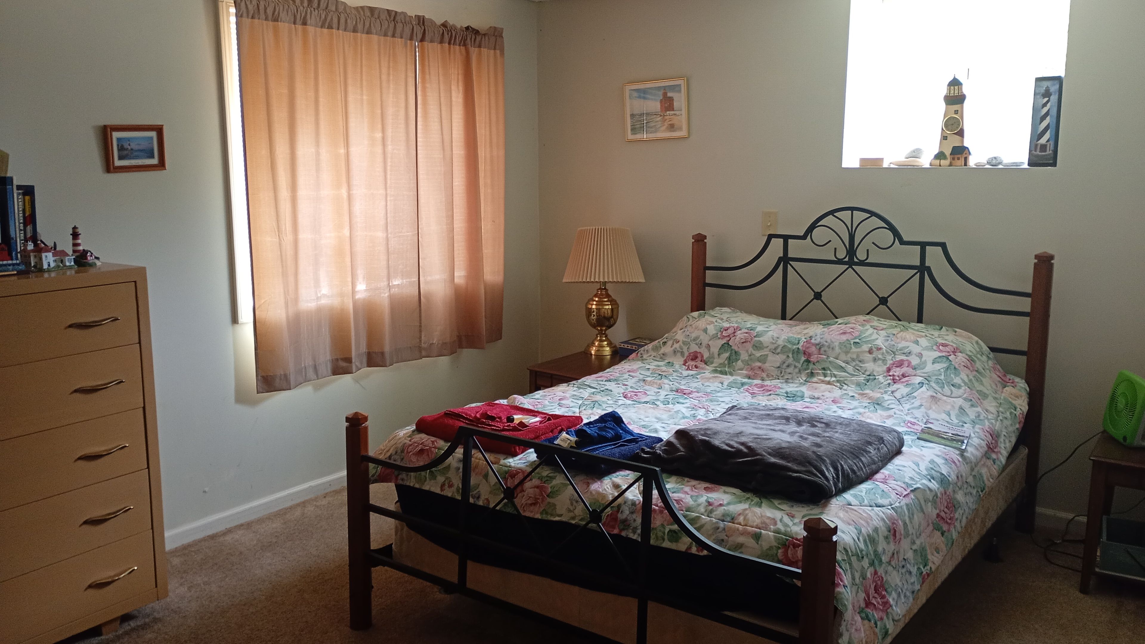 A bedroom with a bed, a dresser, a lamp, and a window with curtains.