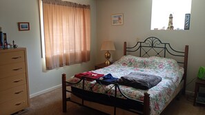 A bedroom with a bed, a dresser, a lamp, and a window with curtains.