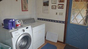 A laundry room with a washing machine, a blue mat, and a door with a window. - Only 1 dollar cleaning fee at Pictured Rocks Basecamp on the Manistique River! (Germfask)