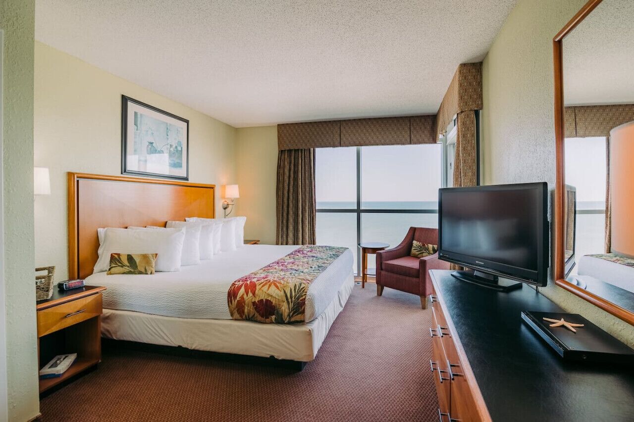 A hotel room with a large bed, a television, a chair, and a view of the sea.