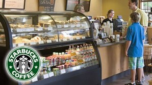Interior de uma cafeteria Starbucks, com uma vitrine de doces e um balcão com cardápio.