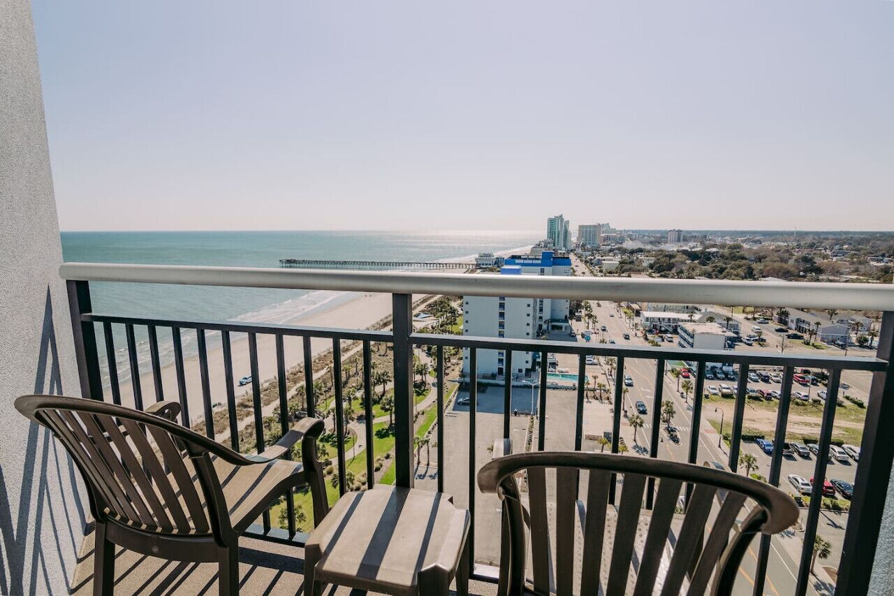 A balcony with two chairs overlooking a beach and a cityscape.