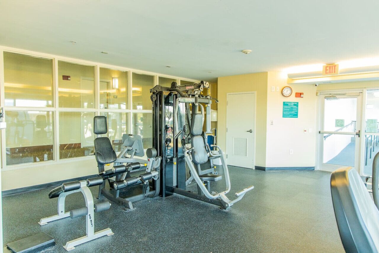 Une salle de sport équipée de machines de musculation, d’un tapis de course et d’un mur recouvert de miroirs.