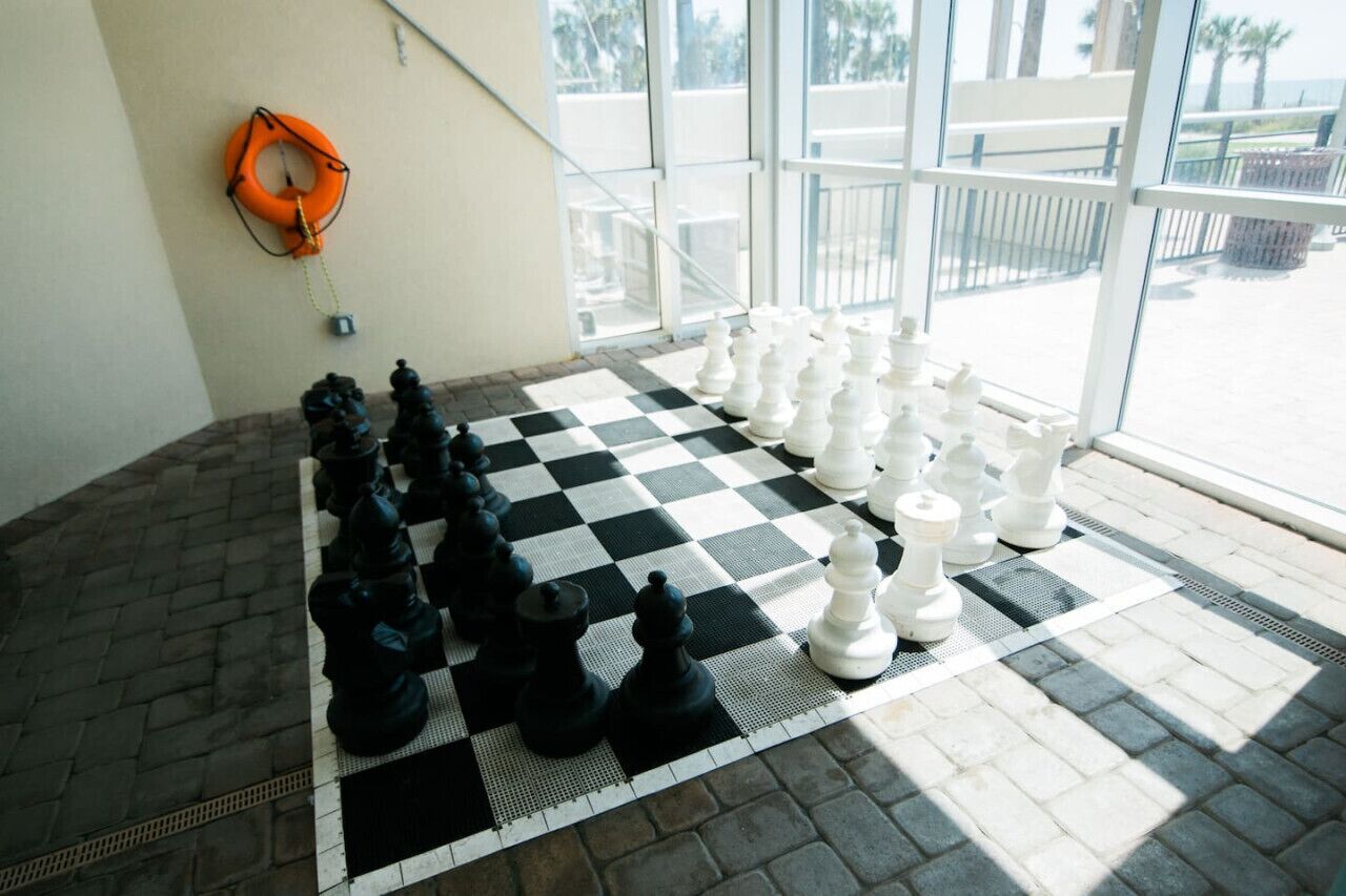 A checkered chessboard with chess pieces set up in a hotel room with large windows and a lifebuoy on the wall.