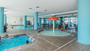 Piscina interior com várias pistas de natação, um elemento central de água e área de estar com mesas e cadeiras.