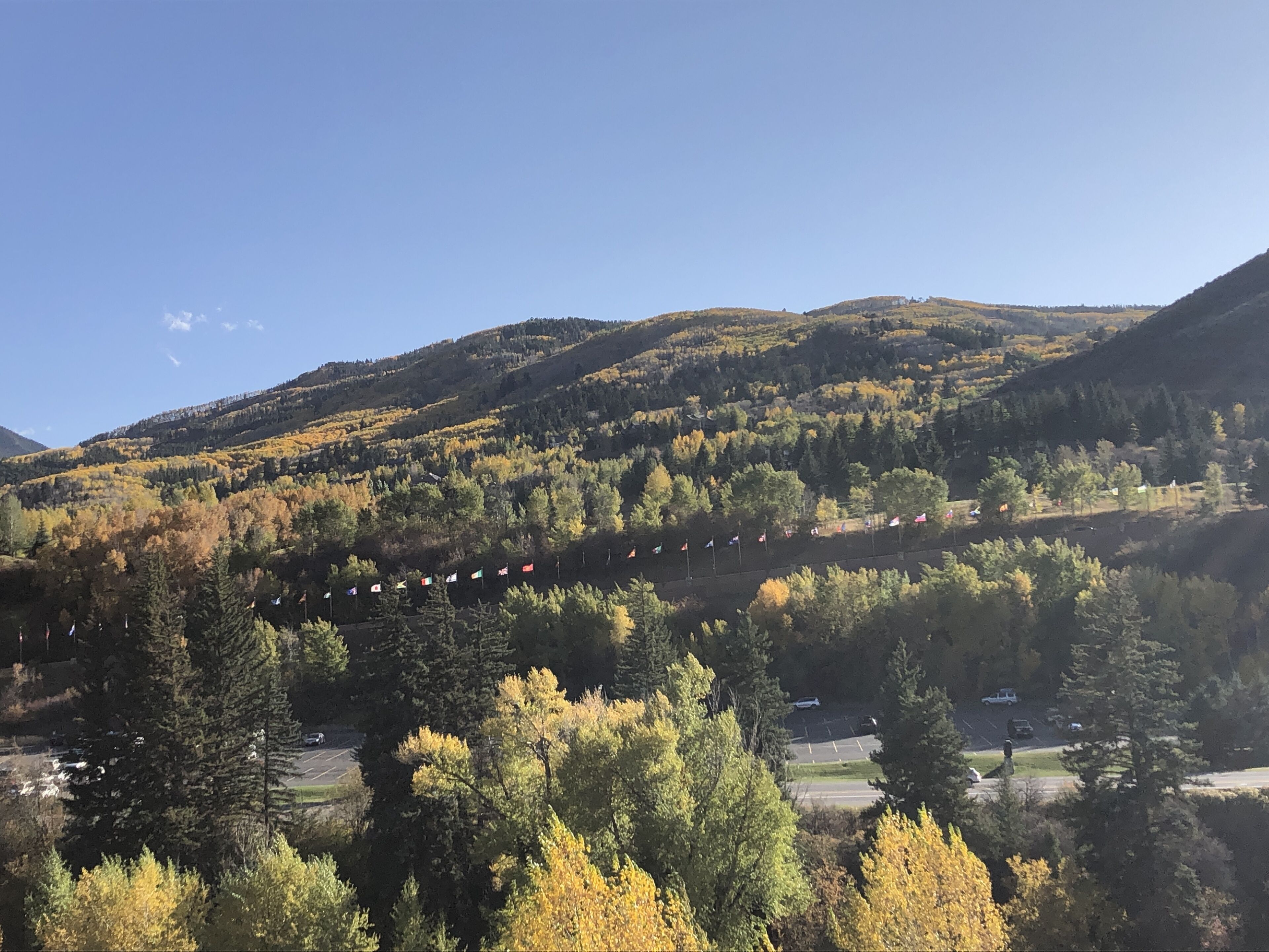 A mountainous landscape with autumn foliage, a parking area, and a road.