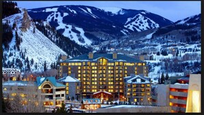 A large hotel with multiple floors and a central atrium, surrounded by snow-covered mountains and a small village. - Luxury Westin Resort and Spa Ski-in/out, sleeps 8, Mountain Views (Avon)