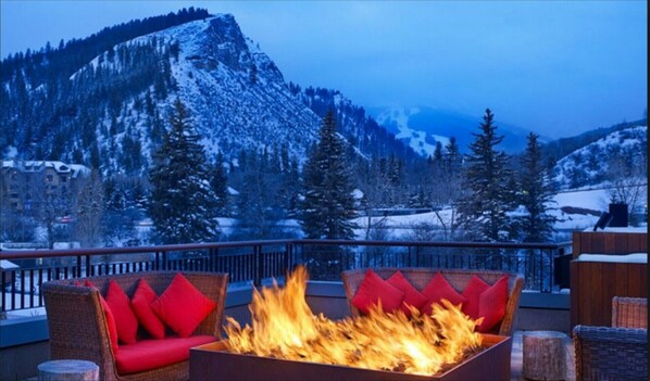 A fire pit with red cushions on a balcony overlooking a snowy mountain landscape.