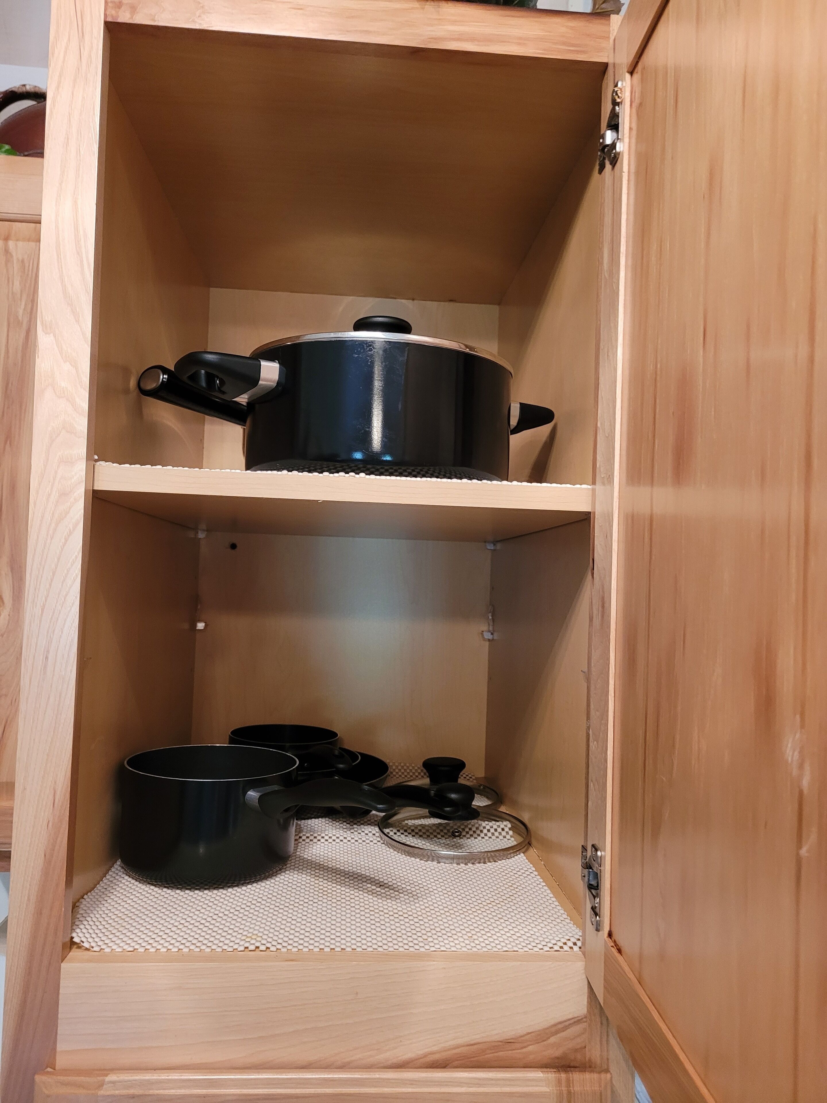 A wooden cabinet with two shelves, one holding a black pot and the other with a black pan and a small pot.
