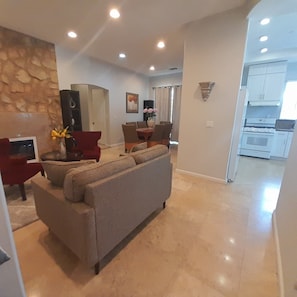A modern living room with a sofa, red chairs, a TV, and a stone wall.