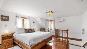 Un dormitorio con una cama de madera, ropa de cama blanca, una mesita de noche, una lámpara y una ventana con cortinas.