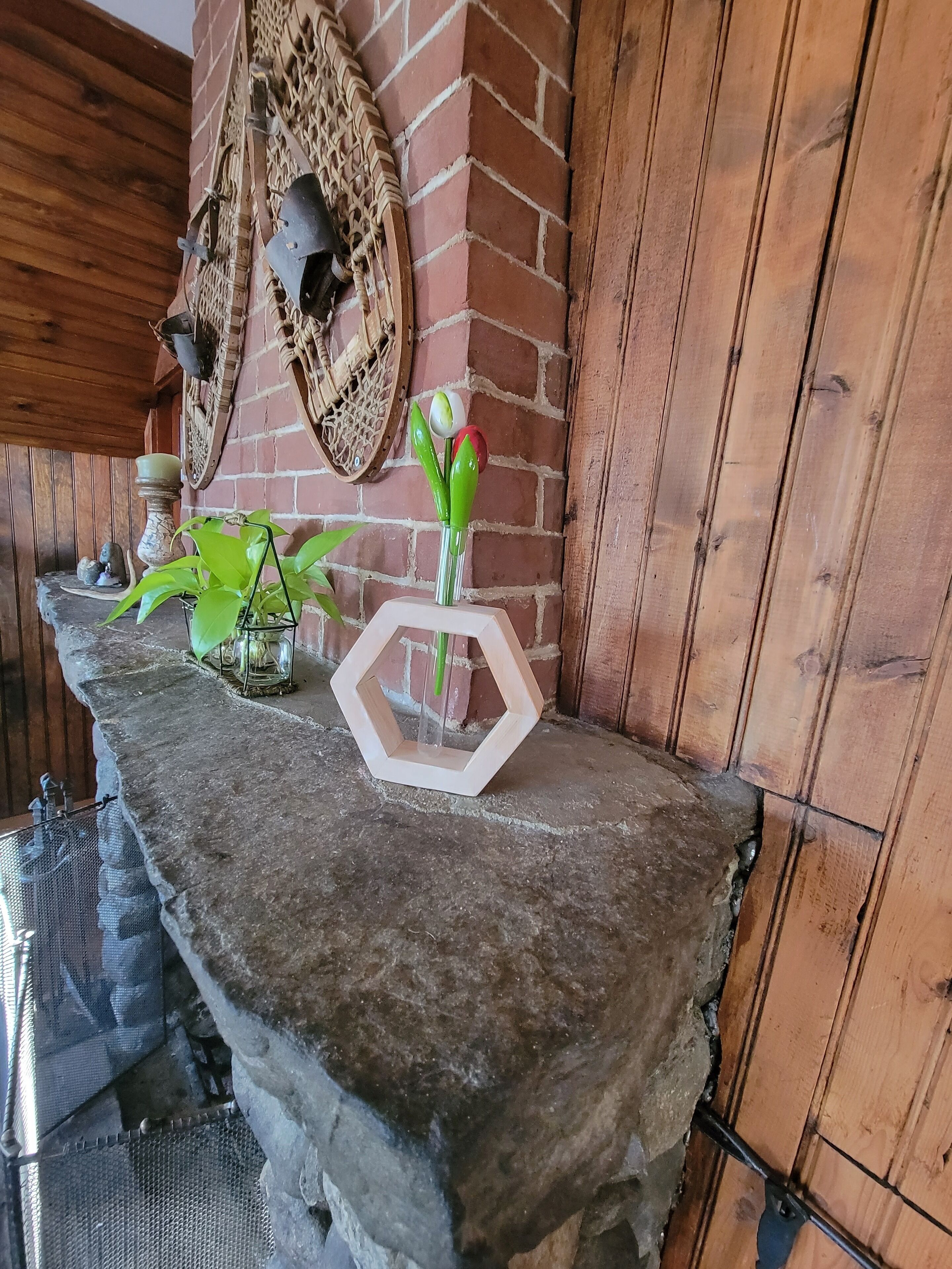 A stone ledge with a hexagonal mirror, a vase with green plants, and a decorative wall piece.