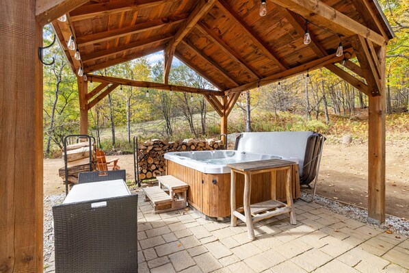 A wooden outdoor hot tub area with a pergola roof, a hot tub, wooden seating, and a fire pit.