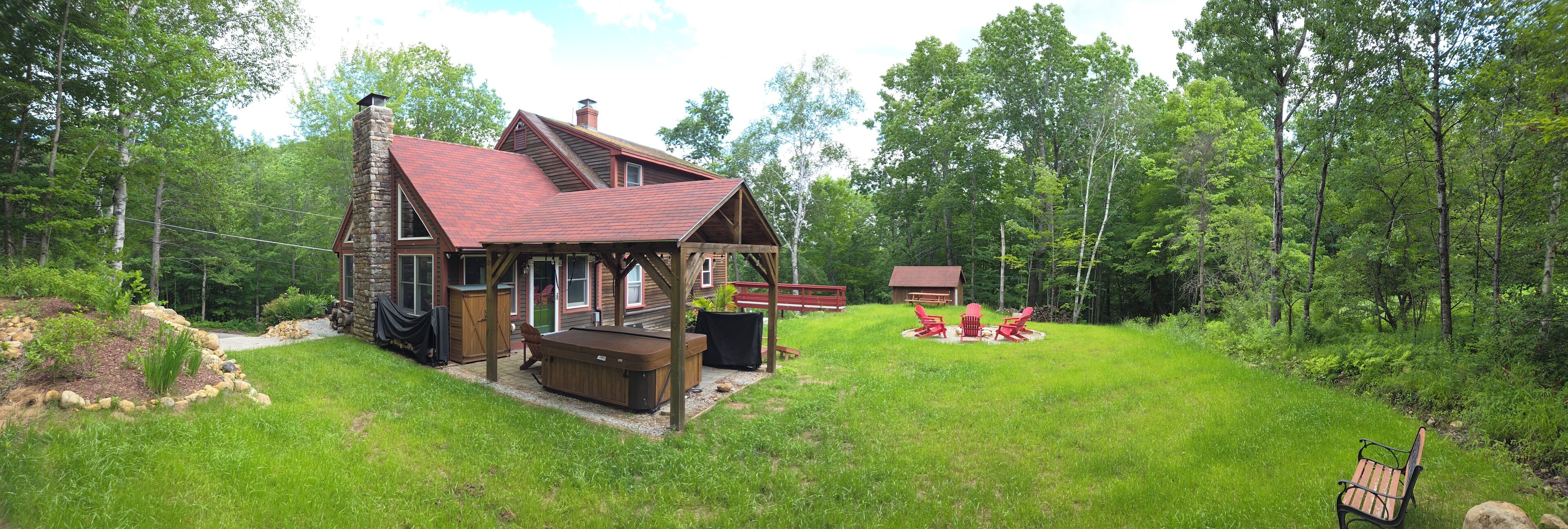 A rustic cabin with a stone chimney, a deck, and a hot tub.