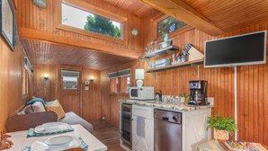 A wooden cabin interior with a dining area, kitchen, and a TV mounted on the wall.