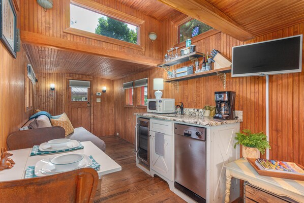 Interior de una cabaña de madera con comedor, cocina y televisor montado en la pared.