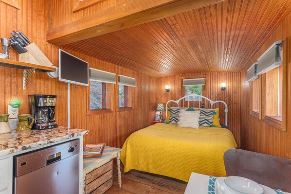 A wooden cabin interior with a bed, a kitchen area, and a dining table.