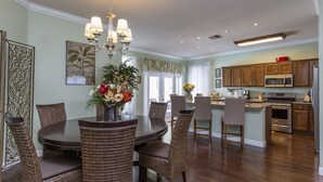 A dining area with a round table and wicker chairs, a kitchen with wooden cabinets and stainless steel appliances, and a chandelier. - Family Disney Villa w/private pool 15 min to Parks (Davenport)