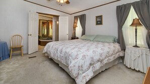 A bedroom with a bed, a chair, a vanity, and a window with curtains.