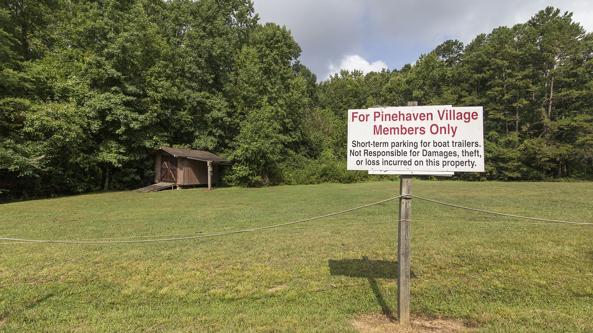 A sign for Pinehaven Village Members Only with a wooden structure in the background.