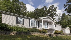 A two-story mobile home with a porch and a stone retaining wall.