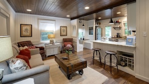 A spacious living room with a sofa, coffee table, and a dining area with stools. - Walk to Downtown Cashiers!CharmingSecluded Cottage w/Resort Access –Pet Friendly (Cashiers)