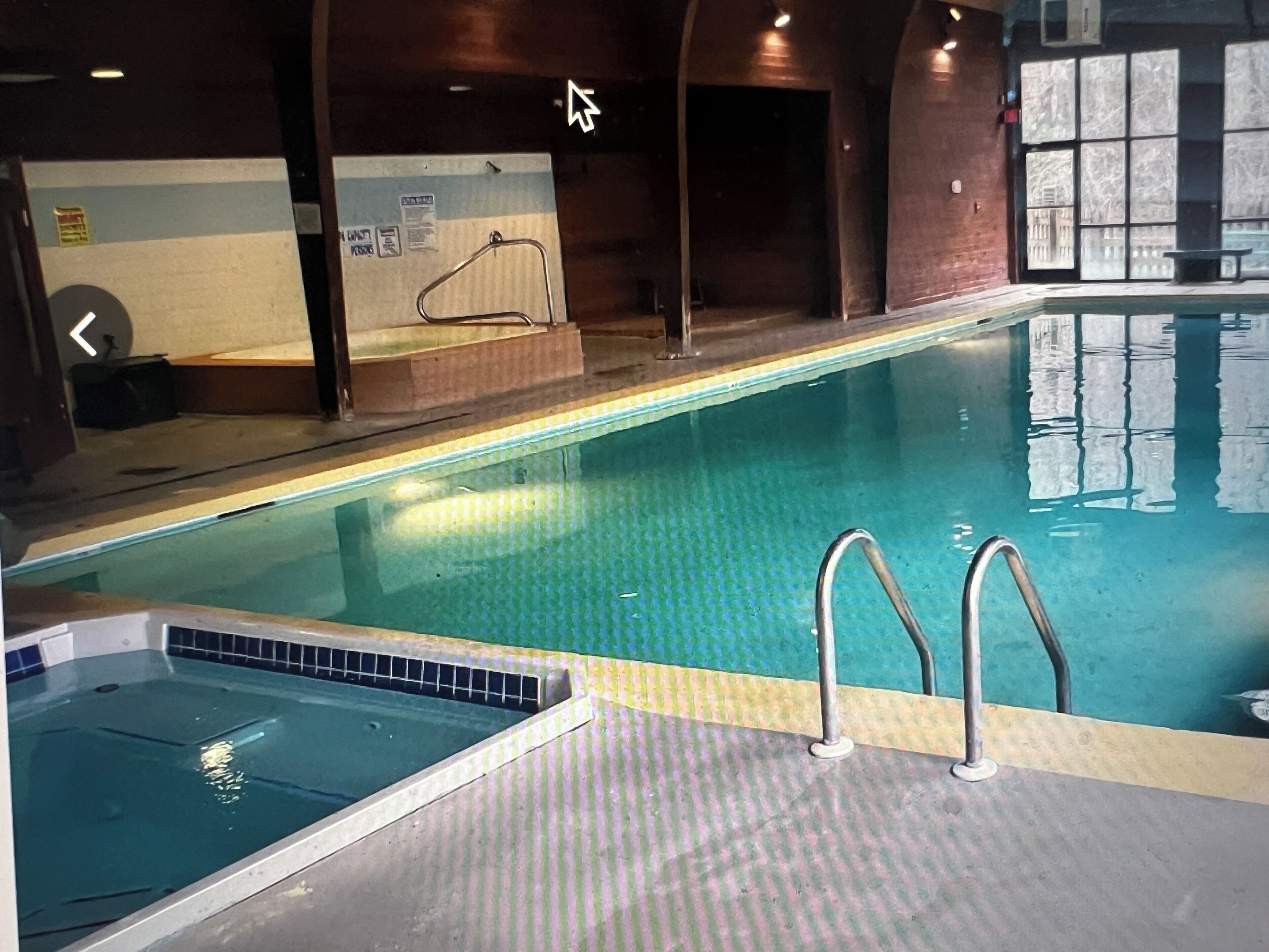 An indoor swimming pool with clear water, a tiled edge, and metal handrails.