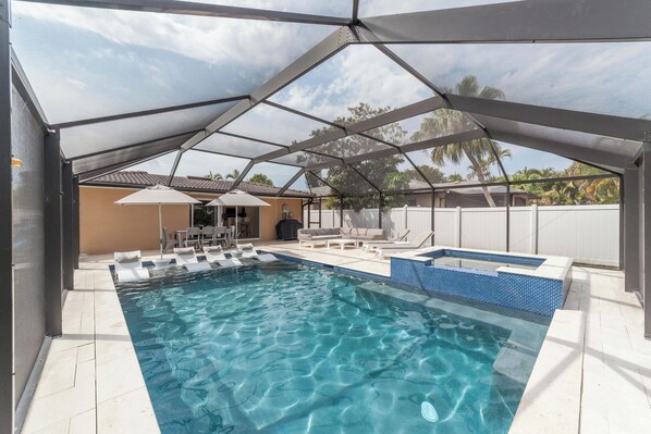 A swimming pool with a shaded area, lounge chairs, and a hot tub.