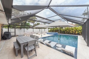 A covered outdoor area with a pool, lounge chairs, and a table with chairs.