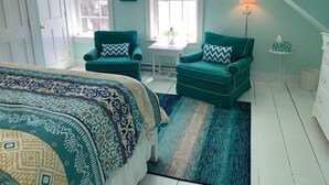Um quarto com uma cama, duas poltronas azul-turquesa, uma mesinha, uma luminária e uma janela com vista.