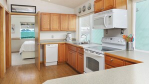 Una cocina compacta con armarios de madera, microondas, cafetera y lavavajillas.