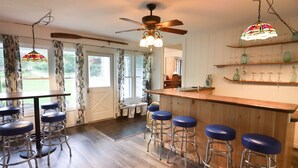 A kitchen with wooden bar stools, a bar counter, and a ceiling fan.