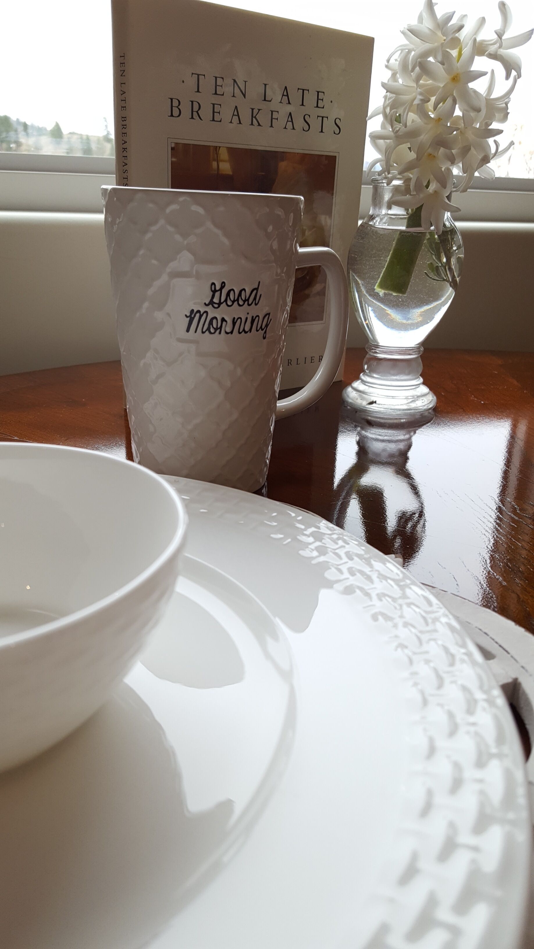 A table with a white mug, a bowl, and a book titled "Ten Late Breakfasts".