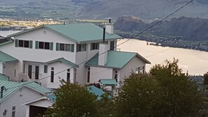 A white building with a green roof, surrounded by trees and overlooking a body of water. - Private Rental Suite: Million Dollar View From Your Deck On 12 Acre Property (Osoyoos)