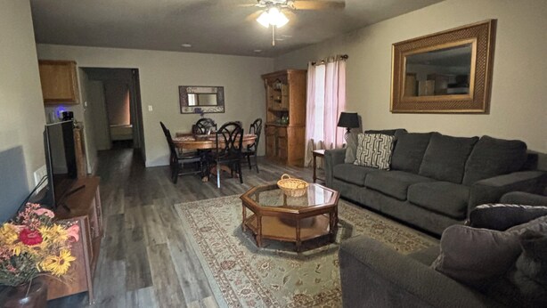 A living room with a sofa, a coffee table, a dining table with chairs, a ceiling fan, and a kitchen area in the background. - 1109 S. Boston Pl 3 bedroom, 2 bath house (Russellville)
