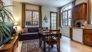 A living room with a sofa, TV, and a dining table with chairs. There is a kitchen area with cabinets and a coffee maker. - Charming, Elegant, Luxury, Walk to Moonlight Beach & Downtown (Encinitas)