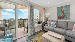 Un balcon spacieux avec vue sur l’océan, un canapé gris agrémenté de coussins décoratifs et un tapis aux couleurs vives.