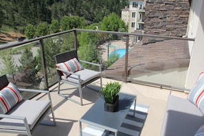 Ein Balkon mit Glasgeländer, zwei Liegestühle, ein kleiner Tisch und ein Blumentopf.