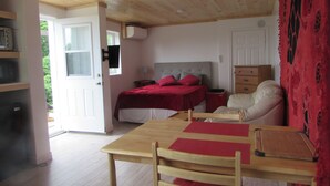 A room with a wooden ceiling, a bed with red bedding, a wooden table, and a chair.