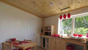 A kitchen with wooden cabinets, a dining table with chairs, and a window with a view of greenery.