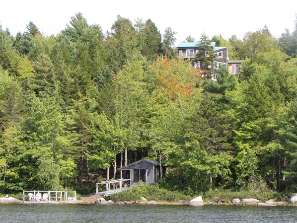 A cabin with a dock extending into a lake, surrounded by dense forest.