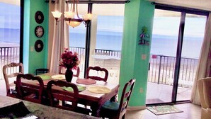 Un coin repas comprenant une table, des chaises, un vase de fleurs et une vue sur l’océan grâce à de grandes portes coulissantes.