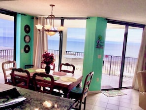 A dining area with a table, chairs, a vase of flowers, and a view of the ocean through large sliding doors.