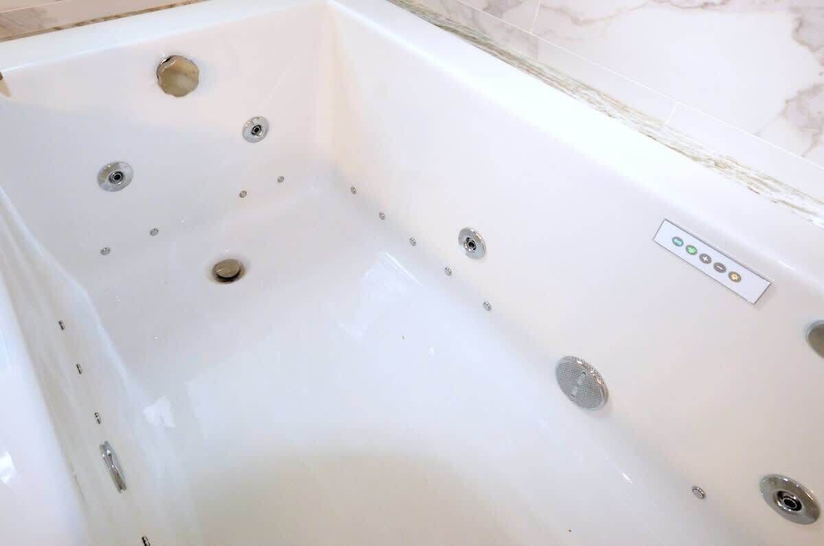 Une baignoire blanche dotée de plusieurs jets, d’un panneau de commande et d’un drain.