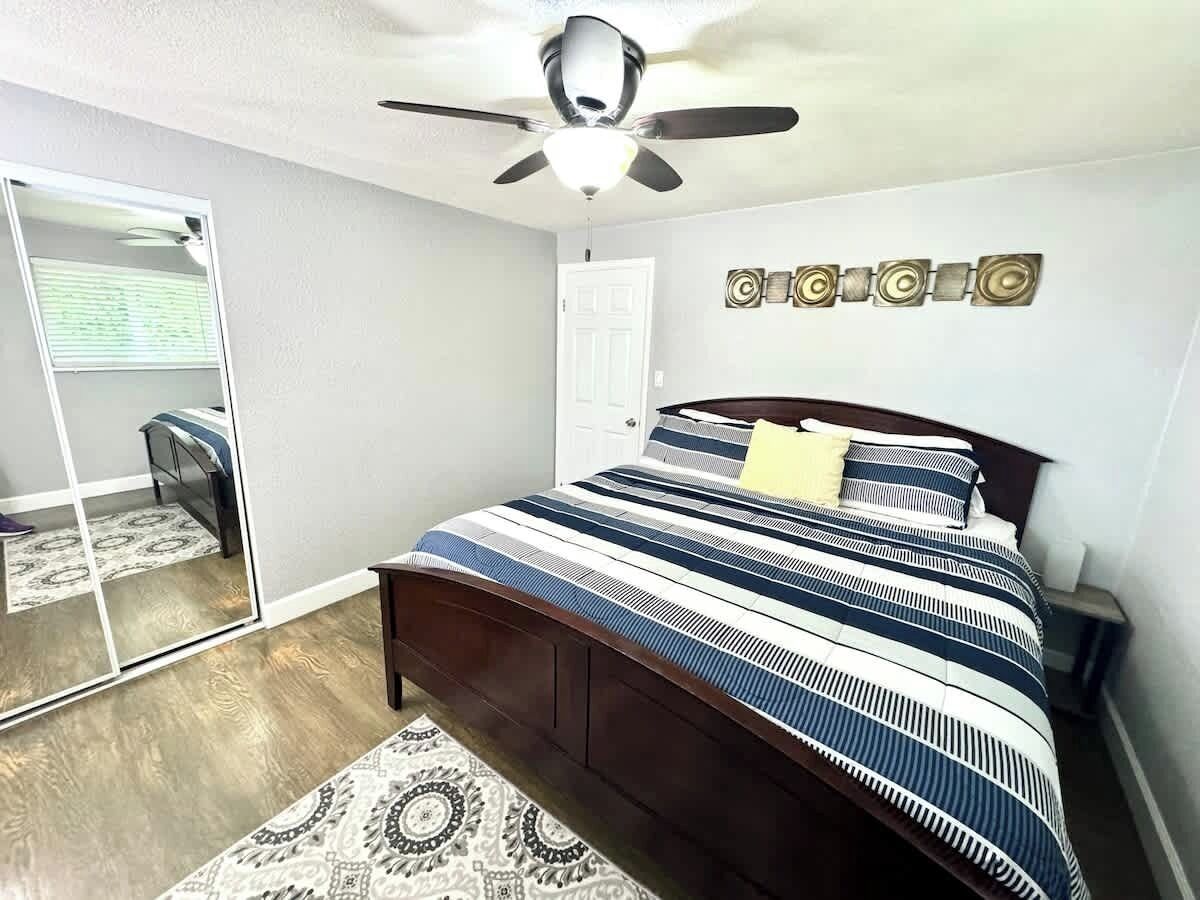 A bedroom with a bed, a ceiling fan, a door, and a mirror.