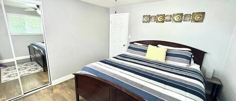 A bedroom with a bed, a ceiling fan, a door, and a mirror.