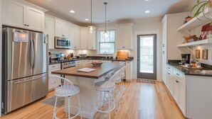 Una cocina moderna con armarios blancos, electrodomésticos de acero inoxidable, una isla central con taburetes y un amplio ventanal que proporciona luz natural.