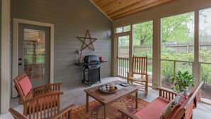 Un patio cubierto con una parrilla, mobiliario de madera y grandes ventanales con vistas a un jardín.
