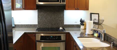 A modern kitchen with wooden cabinets, stainless steel appliances, and a granite countertop.