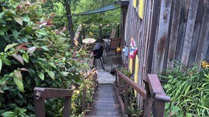A wooden staircase leading to a building with a yellow door, surrounded by greenery. - Rustic, Artsy & Cozy Getaway Cabin in Laurel Highlands- minutes from Ligonier  (Ligonier)